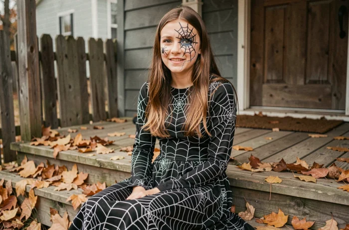 Adolescente en costume d'Halloween avec maquillage toile d'araignée noir autour de l'œil sur un porche en bois
